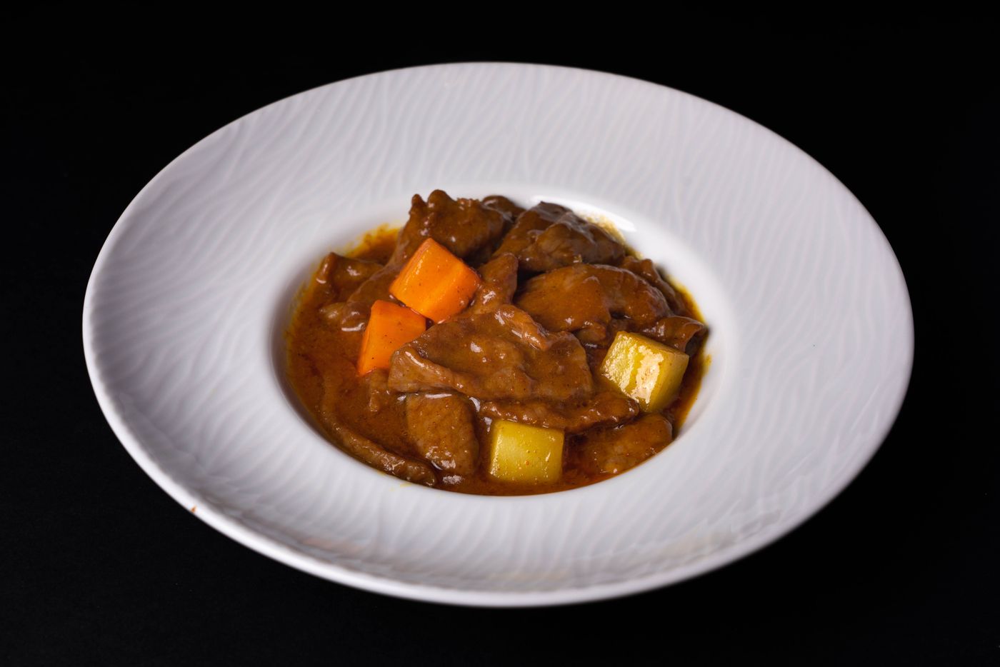 Beef stew with potatoes and carrots. large beef pieces; potato chunks; orange carrot chunks; thick brown gravy.
