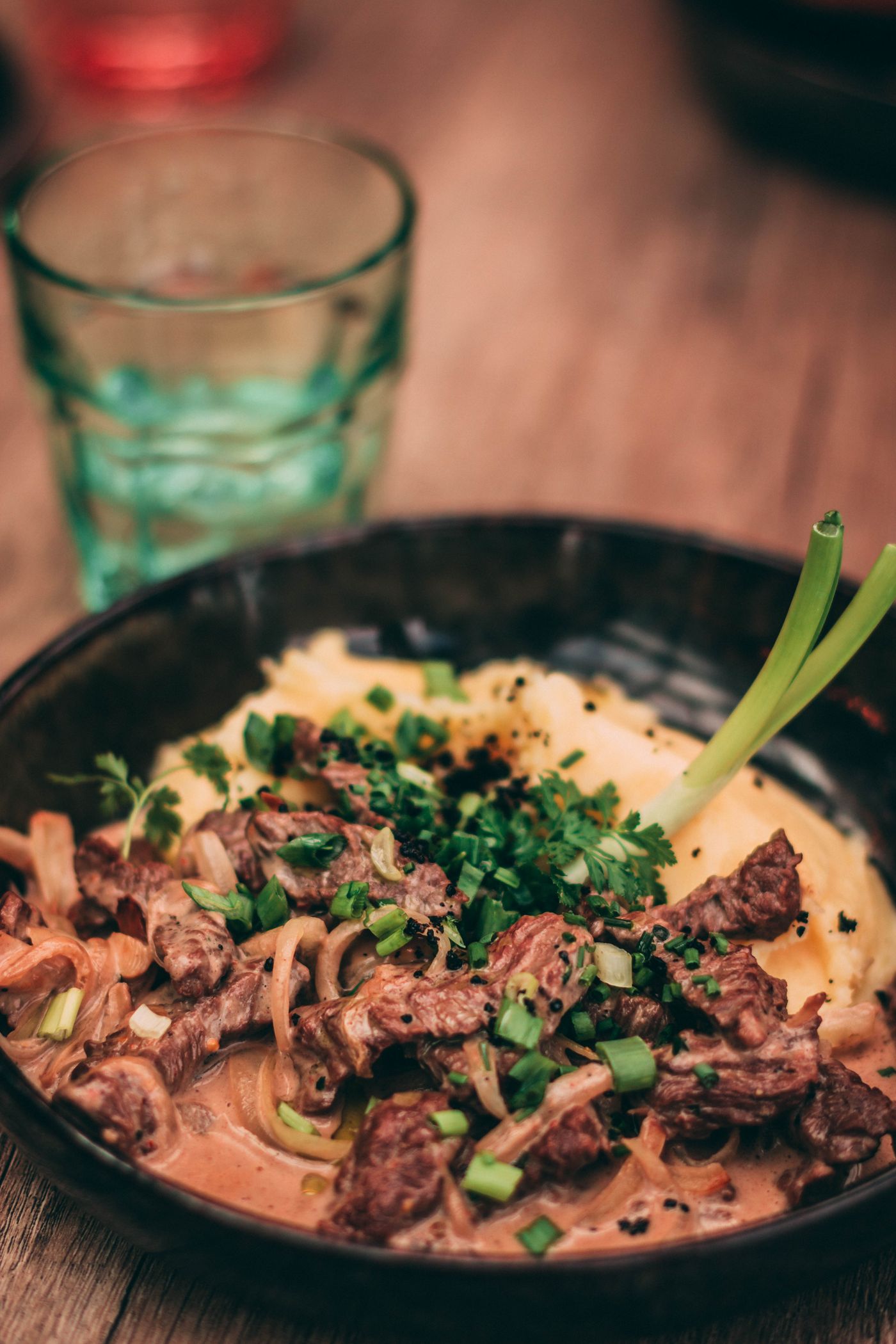 Beef stroganoff with mashed potatoes. beef strips; sliced mushrooms; creamy brown sauce; pale mashed potatoes; sliced scallions; parsley.