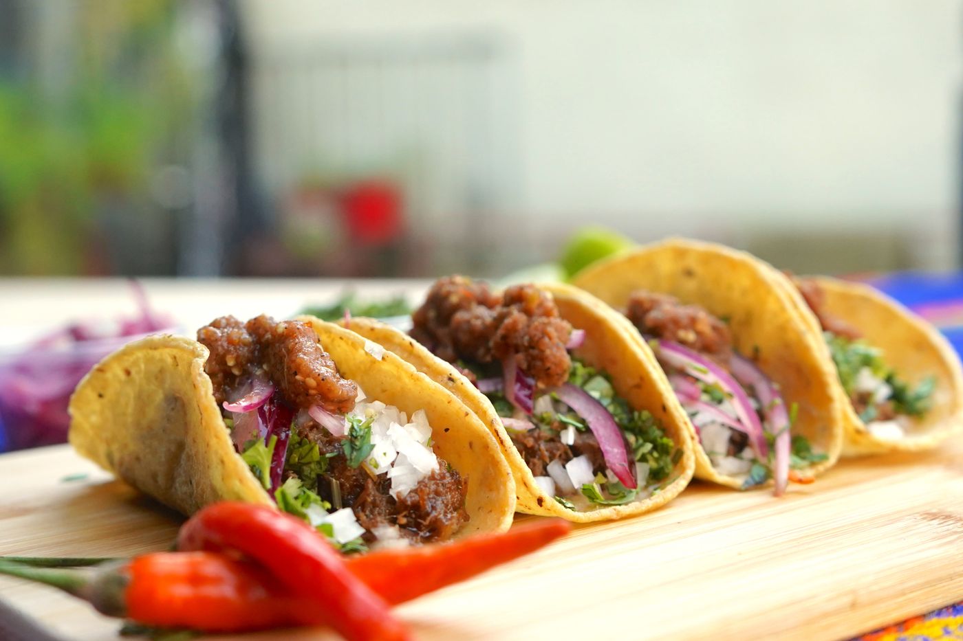 Beef tacos with pickled red onion. golden corn tortillas; chopped browned beef; pink-red onion strips; cilantro; crumbled white cheese.