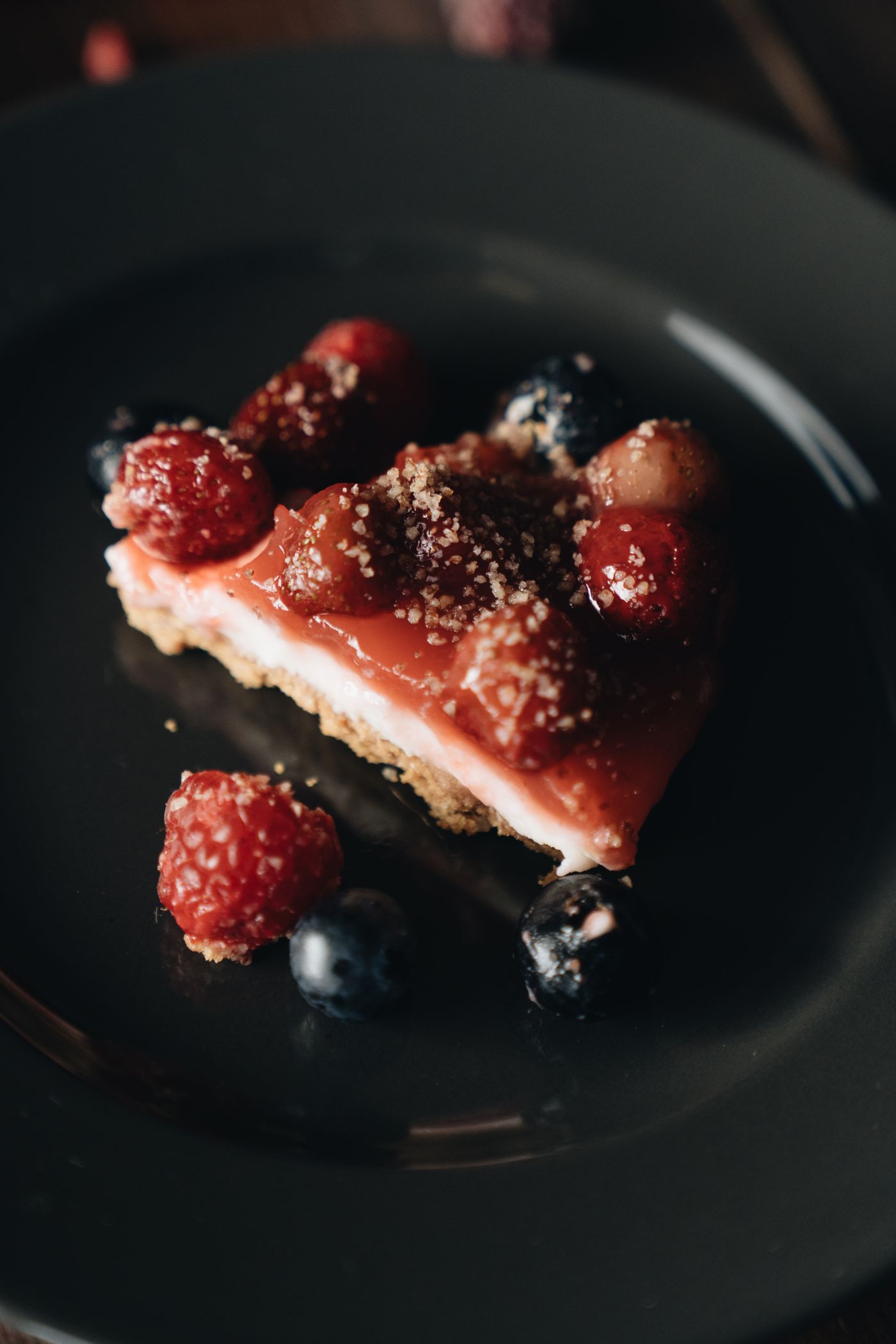 Berry-topped cheesecake slice on a dark plate