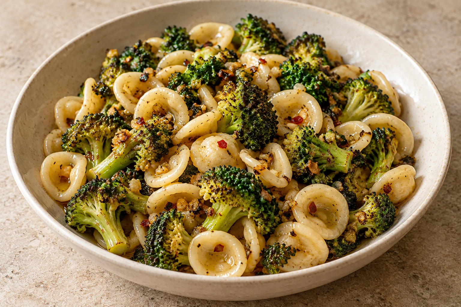 orecchiette with browned roasted broccoli, golden garlic pieces and sparse chili flakes in a shallow cream bowl.