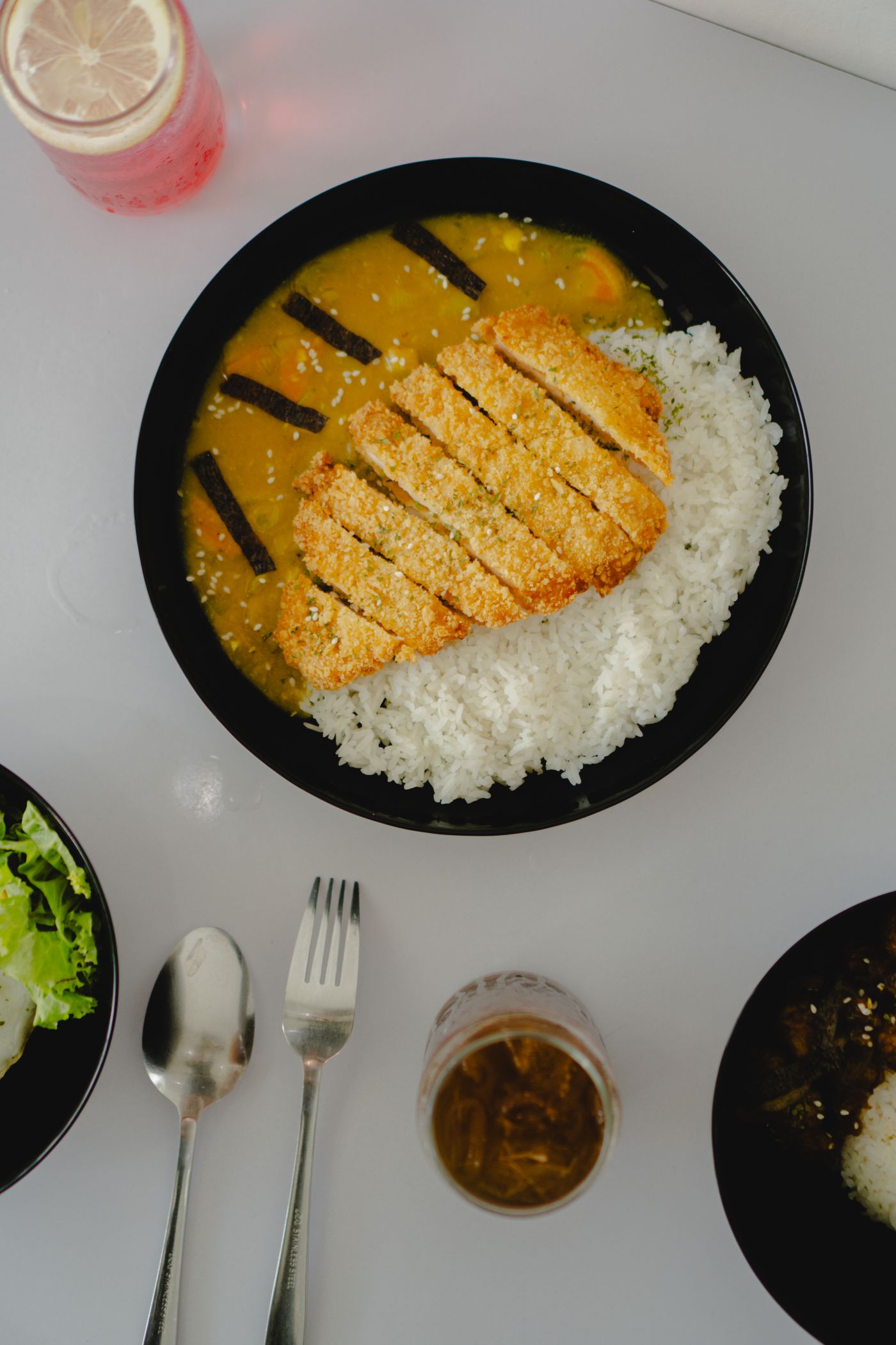 Chicken katsu curry with rice. sliced breaded chicken cutlet; white rice; yellow curry sauce; carrot pieces; dark nori strips; white sesame seeds.