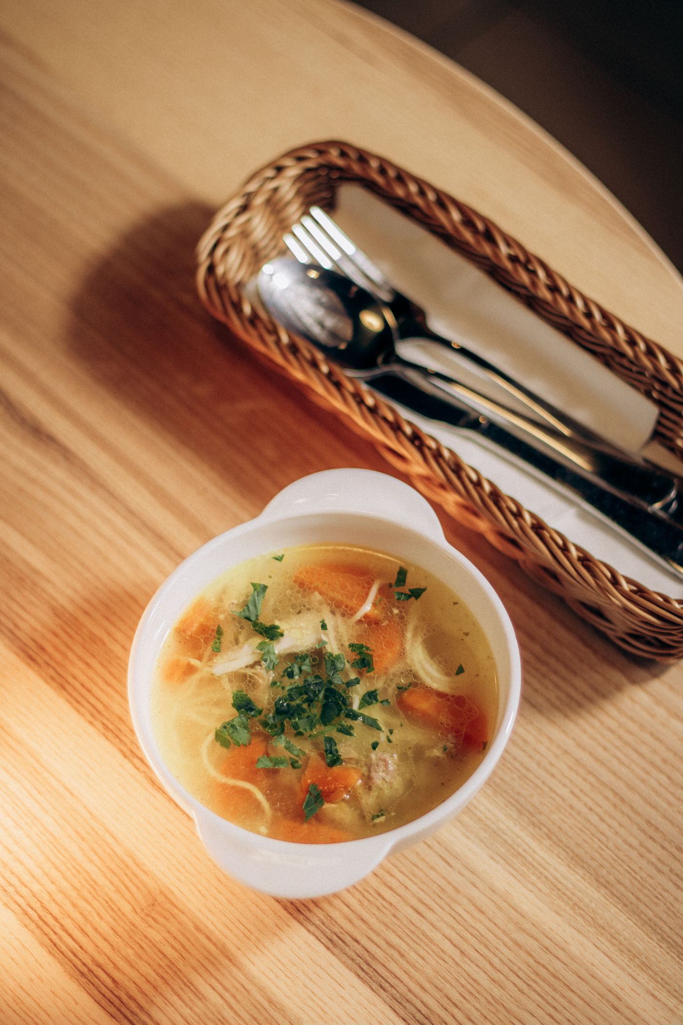 Chicken noodle soup with carrots. thin noodles; carrot pieces; shredded chicken; clear golden broth; chopped leafy herbs.
