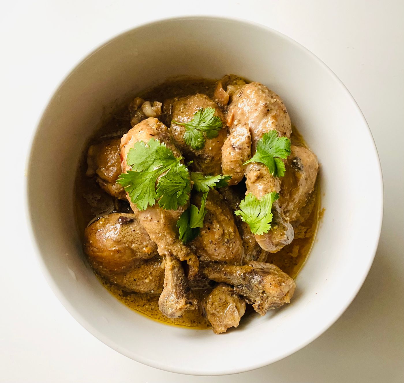 Chicken curry with cilantro. bone-in chicken pieces; thick golden-brown sauce; cilantro leaves.