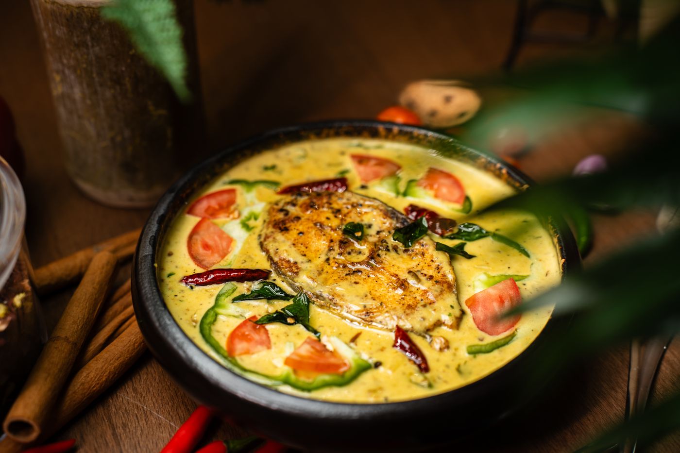 Golden fish curry with tomatoes and peppers. round bone-in fish steak; yellow creamy sauce; tomato wedges; green pepper strips; dried red chilies.