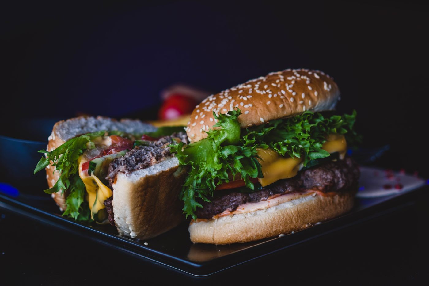 Double cheeseburgers with lettuce and tomato. two beef patties; yellow melted cheese; sesame bun; curly green lettuce; tomato slices; onion rings.