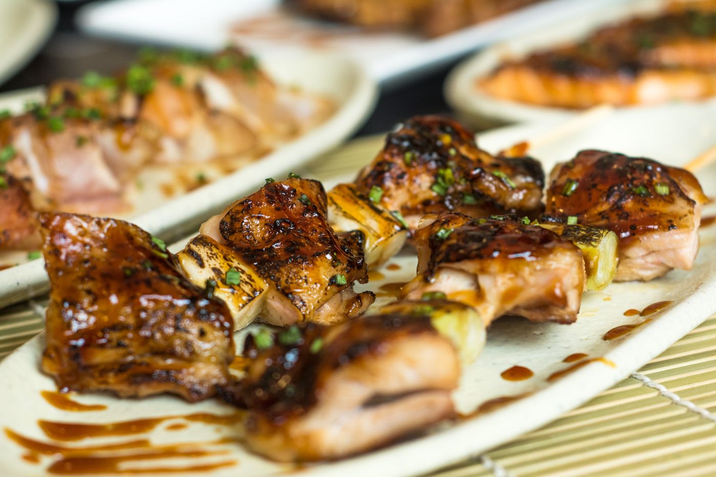 Glazed chicken and scallion skewers. browned chicken pieces; thick pale green scallion sections; dark glossy glaze; finely chopped green garnish.