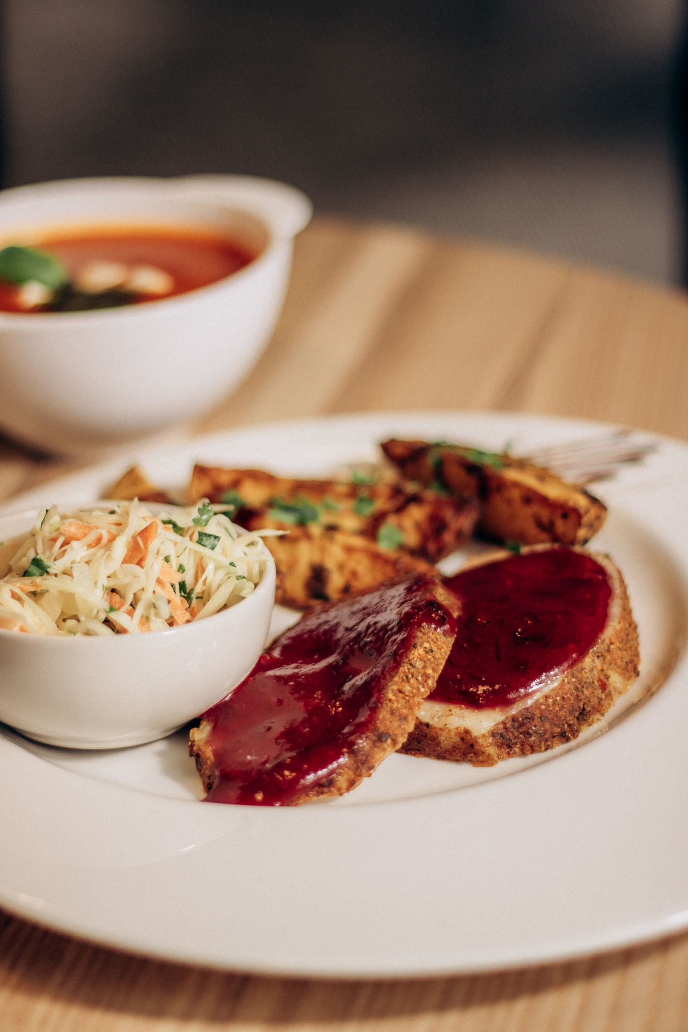 Glazed meatloaf with potato wedges and slaw. two meatloaf slices; glossy dark red glaze; roasted potato wedges; shredded cabbage-carrot slaw.