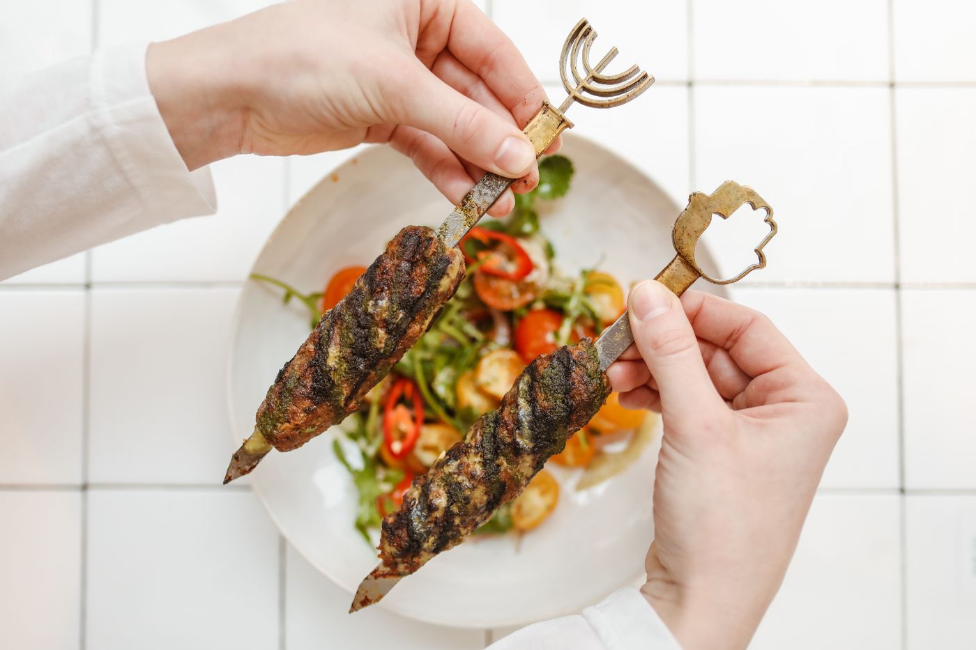Grilled beef kofta with tomato salad. two ridged ground-meat kebabs; red and yellow tomatoes; sliced onion; green herbs.