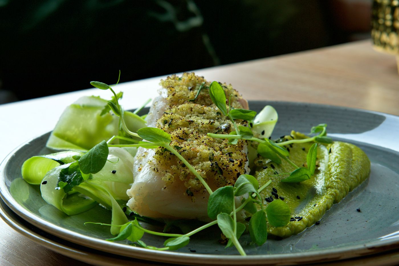 Herb-crusted cod with green vegetable purée. white fish fillet; green herb crumbs; green vegetable purée; shaved pale-green vegetables; pea shoots; green beans or peas.