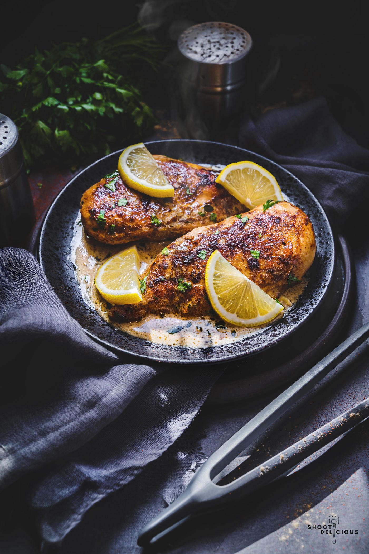 Lemon-garnished roasted chicken breast on a dark plate