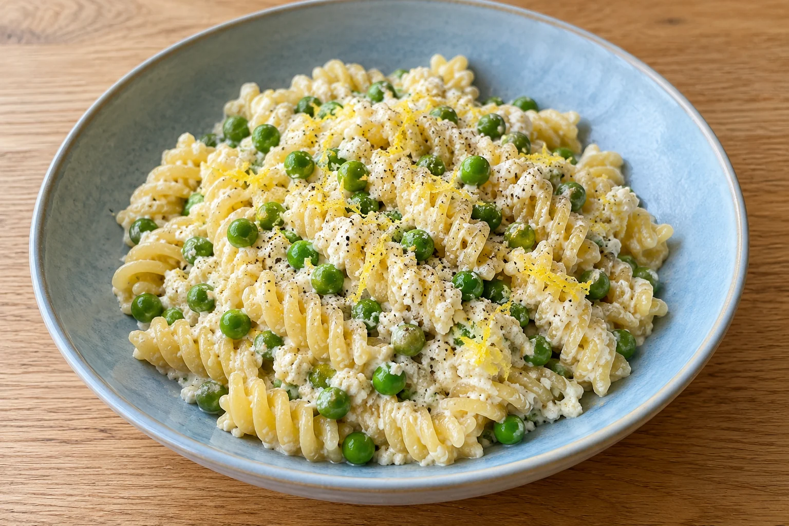 fusilli with green peas, light ricotta-lemon sauce, fine lemon zest and black pepper in a blue bowl.