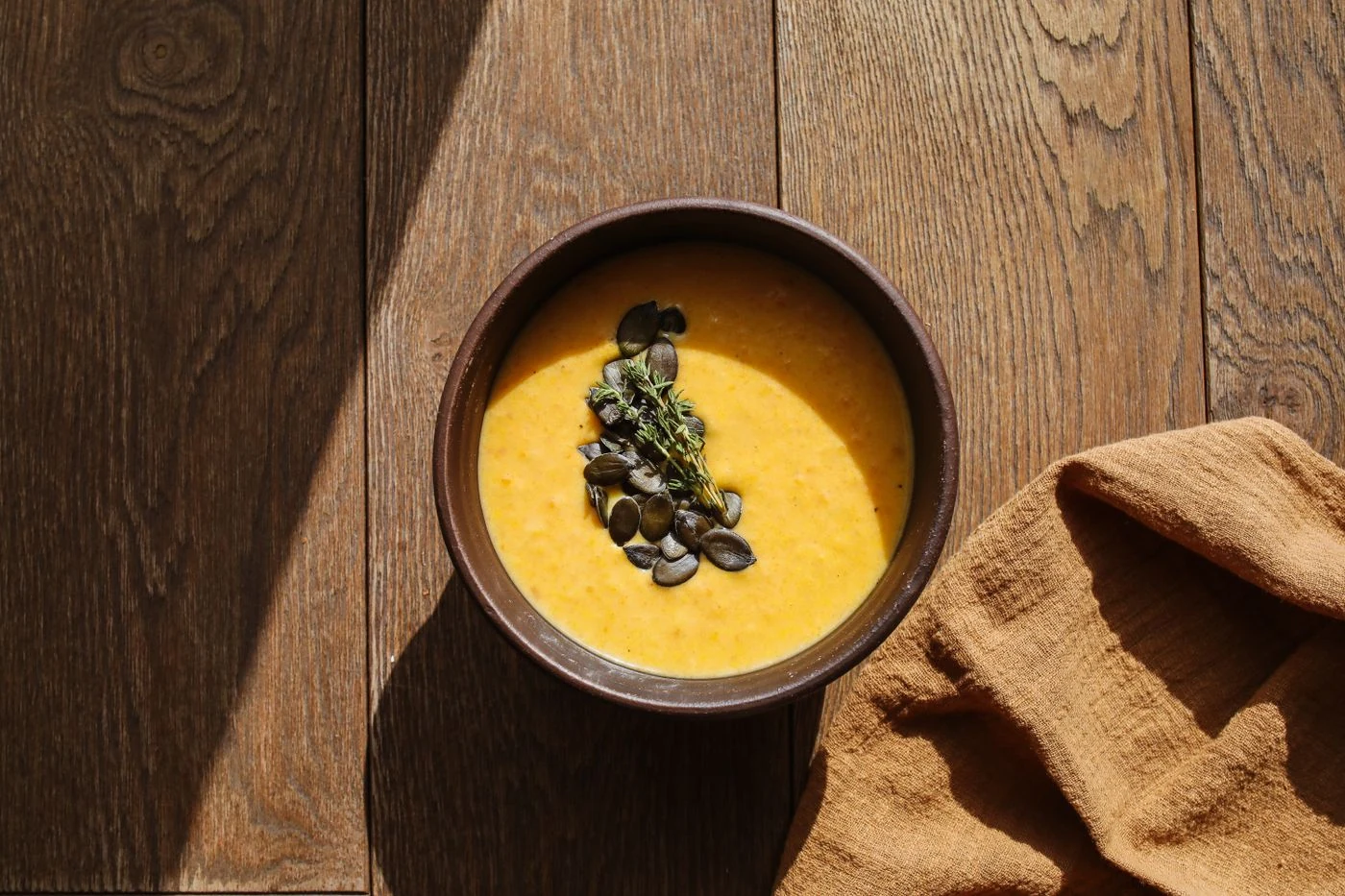 Golden pumpkin soup topped with pumpkin seeds and thyme in a brown bowl