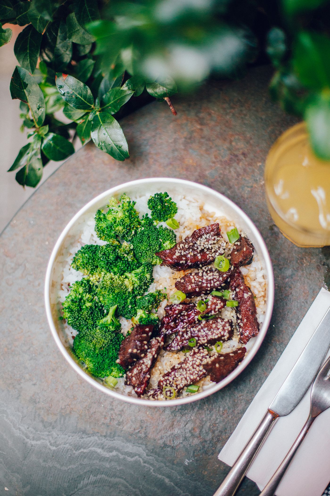Sesame beef and broccoli rice bowls. beef strips; broccoli florets; white rice; white sesame seeds; scallion pieces.
