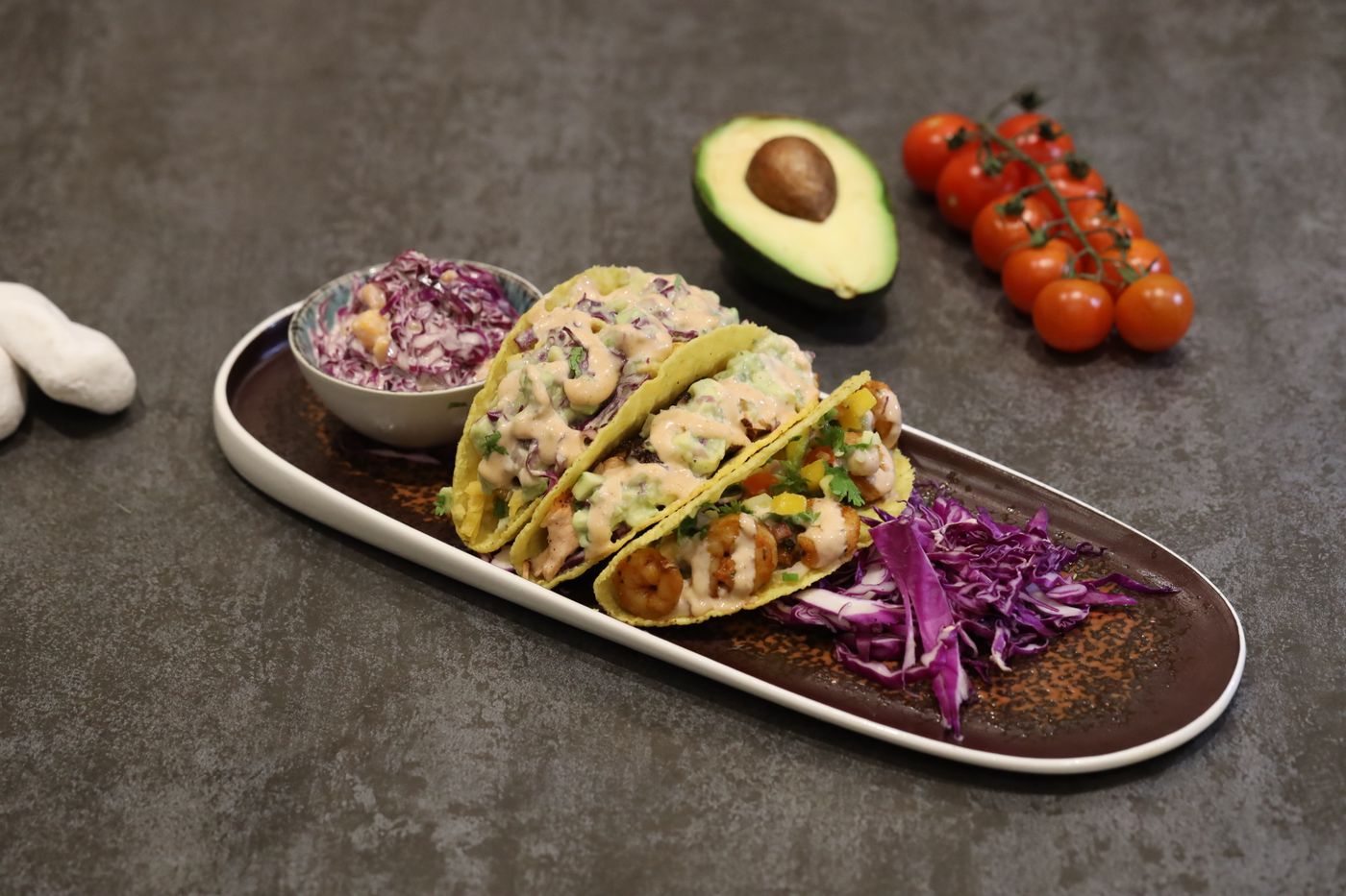 Shrimp tacos with avocado and purple slaw. cooked shrimp; corn tortillas; avocado; shredded purple cabbage; creamy dressing.