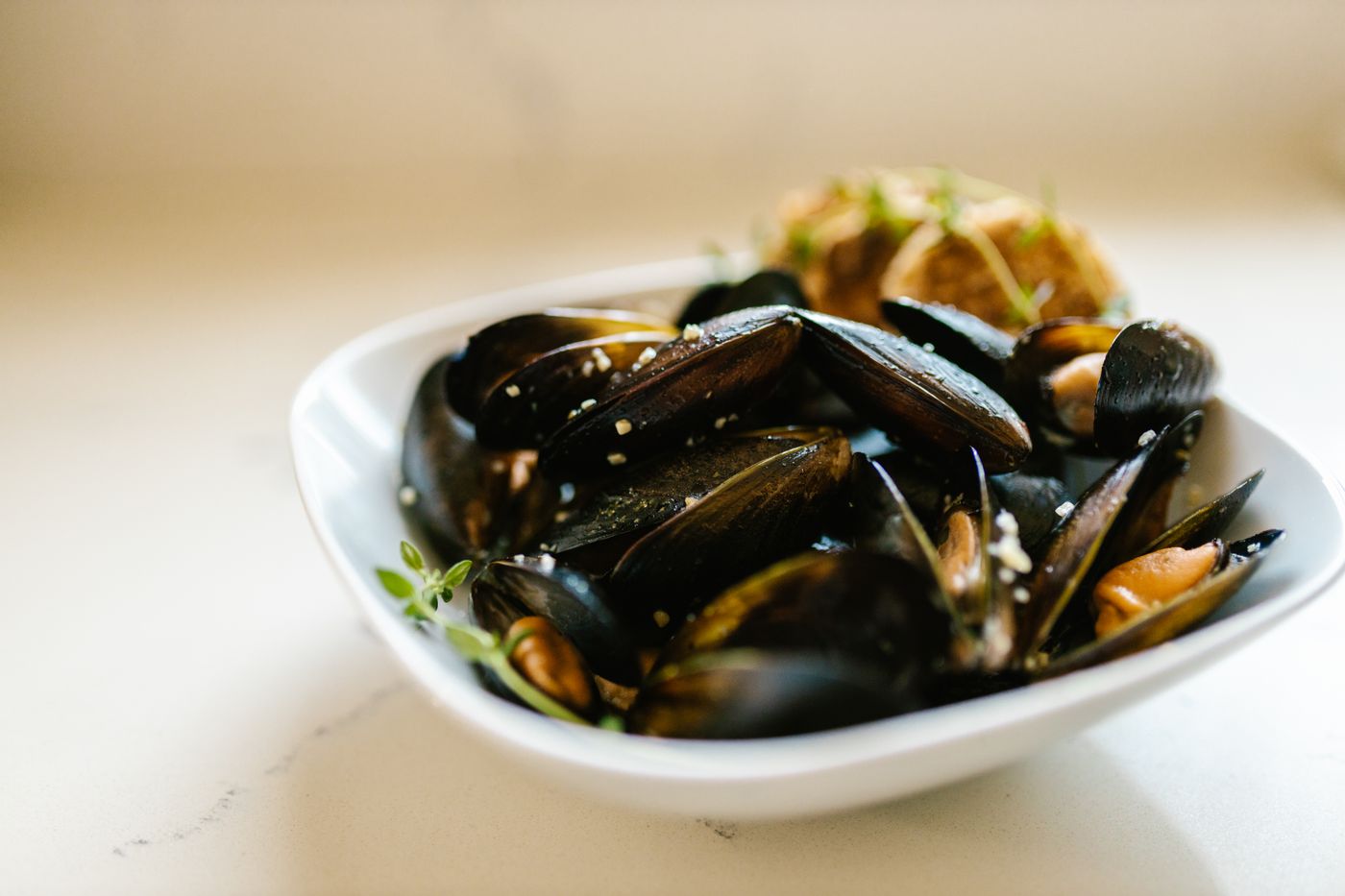 Steamed mussels with herbs. opened black mussel shells; orange mussel flesh; small chopped green herbs; broth.