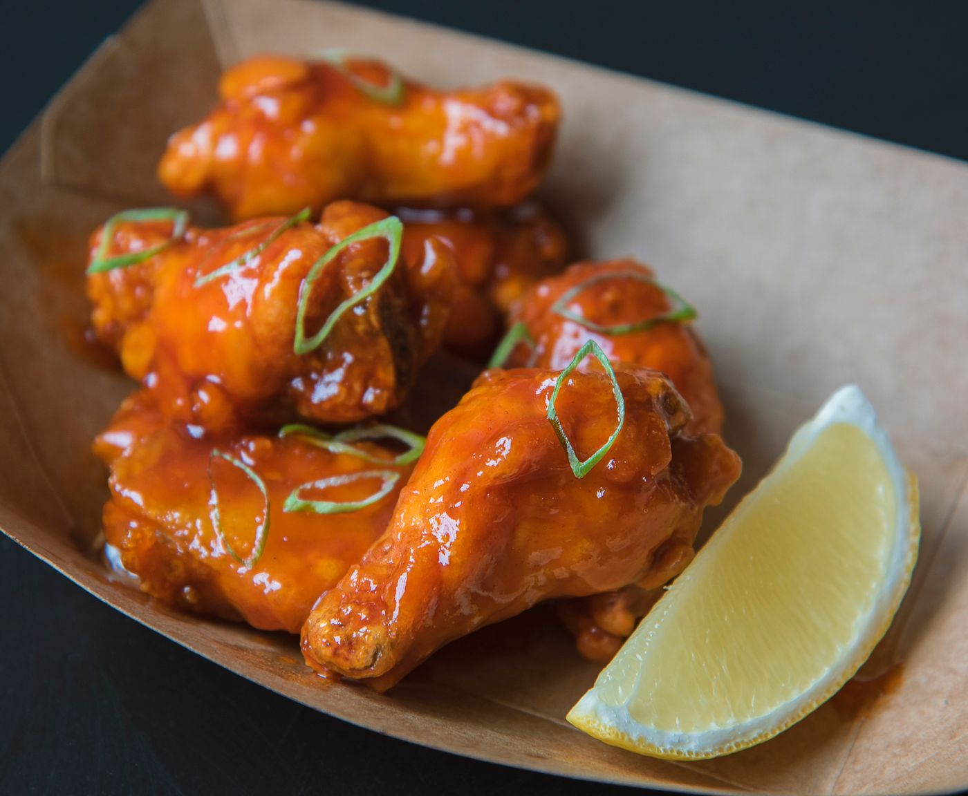 Sticky chicken wings with scallions. glazed chicken wings; thin green scallion rings; lemon wedge.