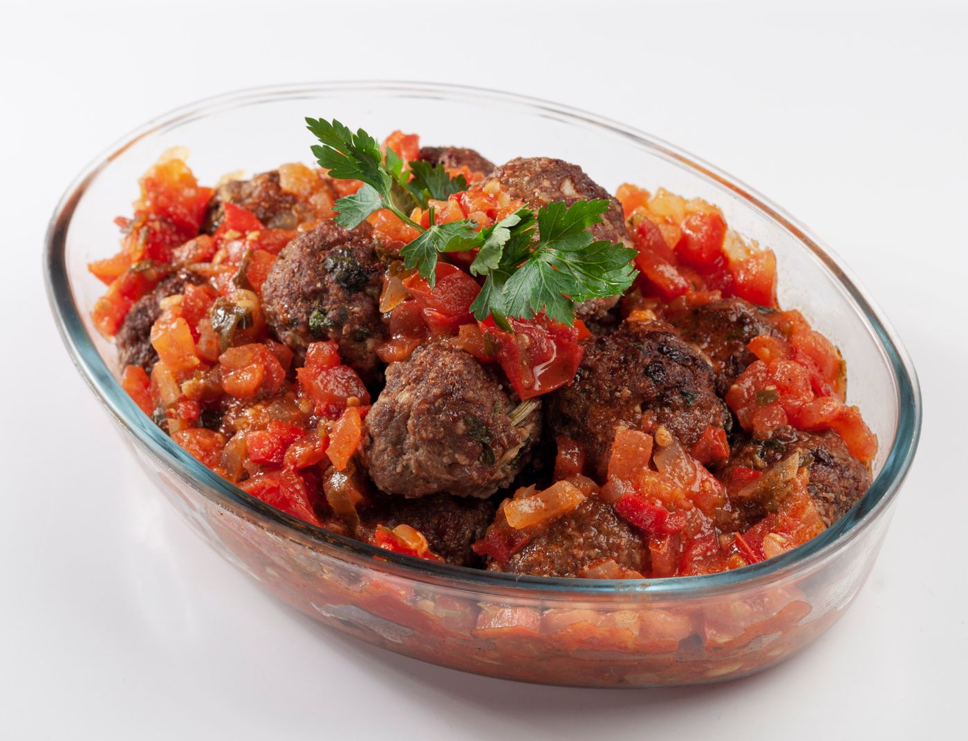 Beef meatballs in chunky tomato sauce. browned meatballs; chopped tomatoes; onion pieces; parsley leaves.