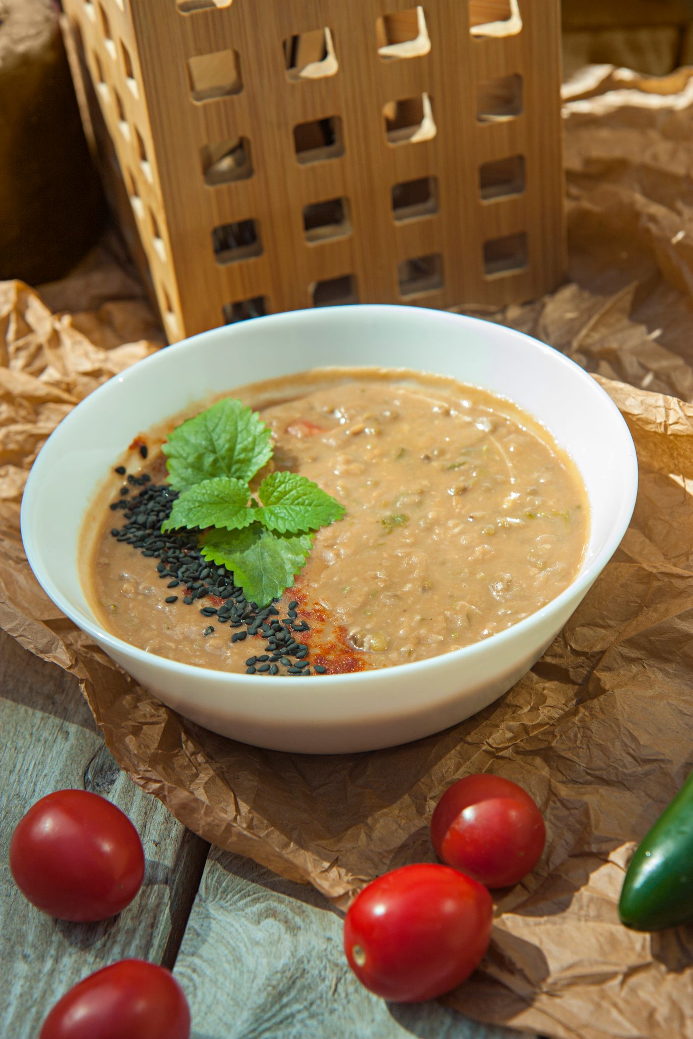 Tomato & red lentil soup; thick orange-brown lentil soup, black sesame seeds, fresh leafy herb garnish, whole tomatoes beside the bowl