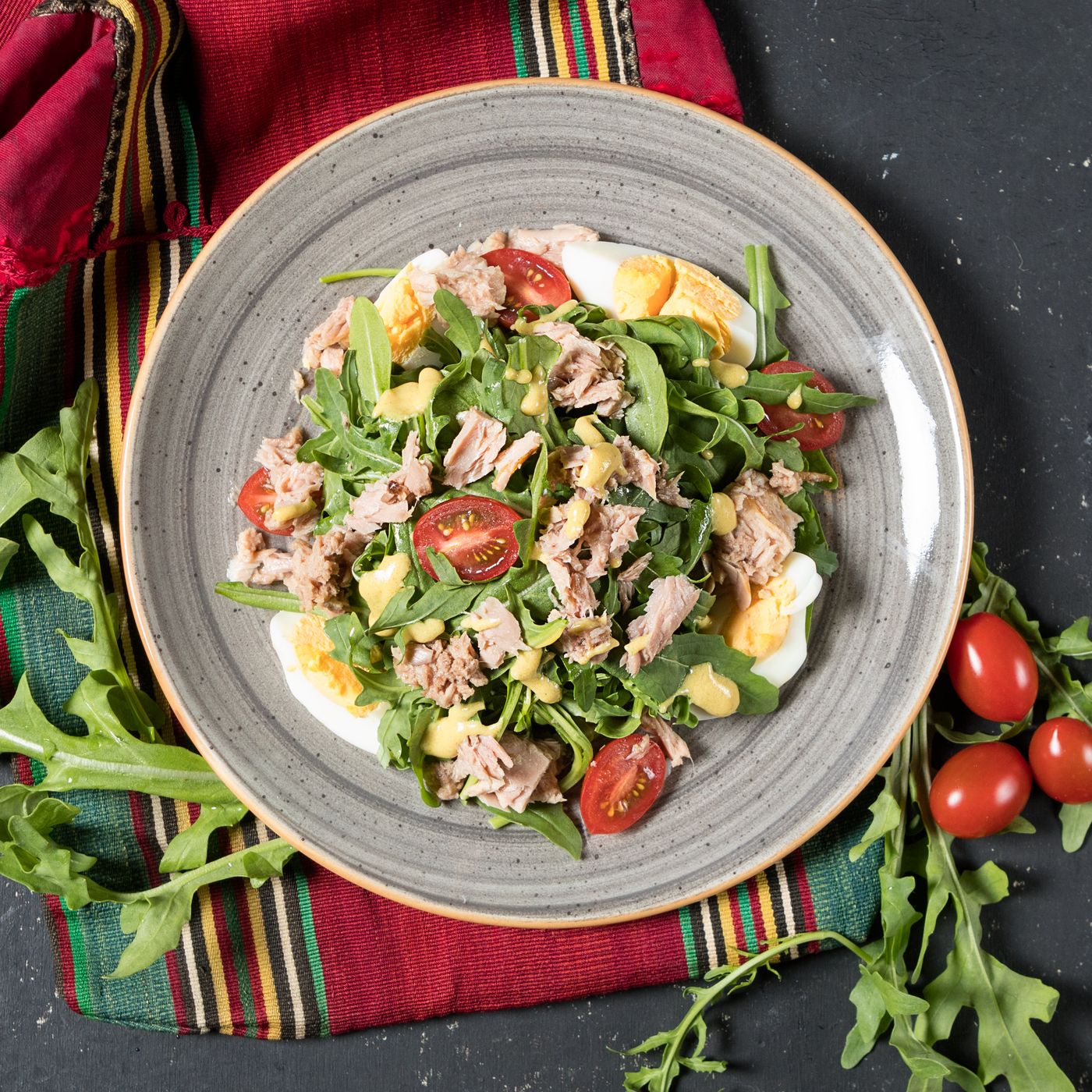 Tuna, egg and arugula salad. flaked tuna; quartered hard-boiled eggs; arugula; cherry tomato halves; pale creamy dressing.