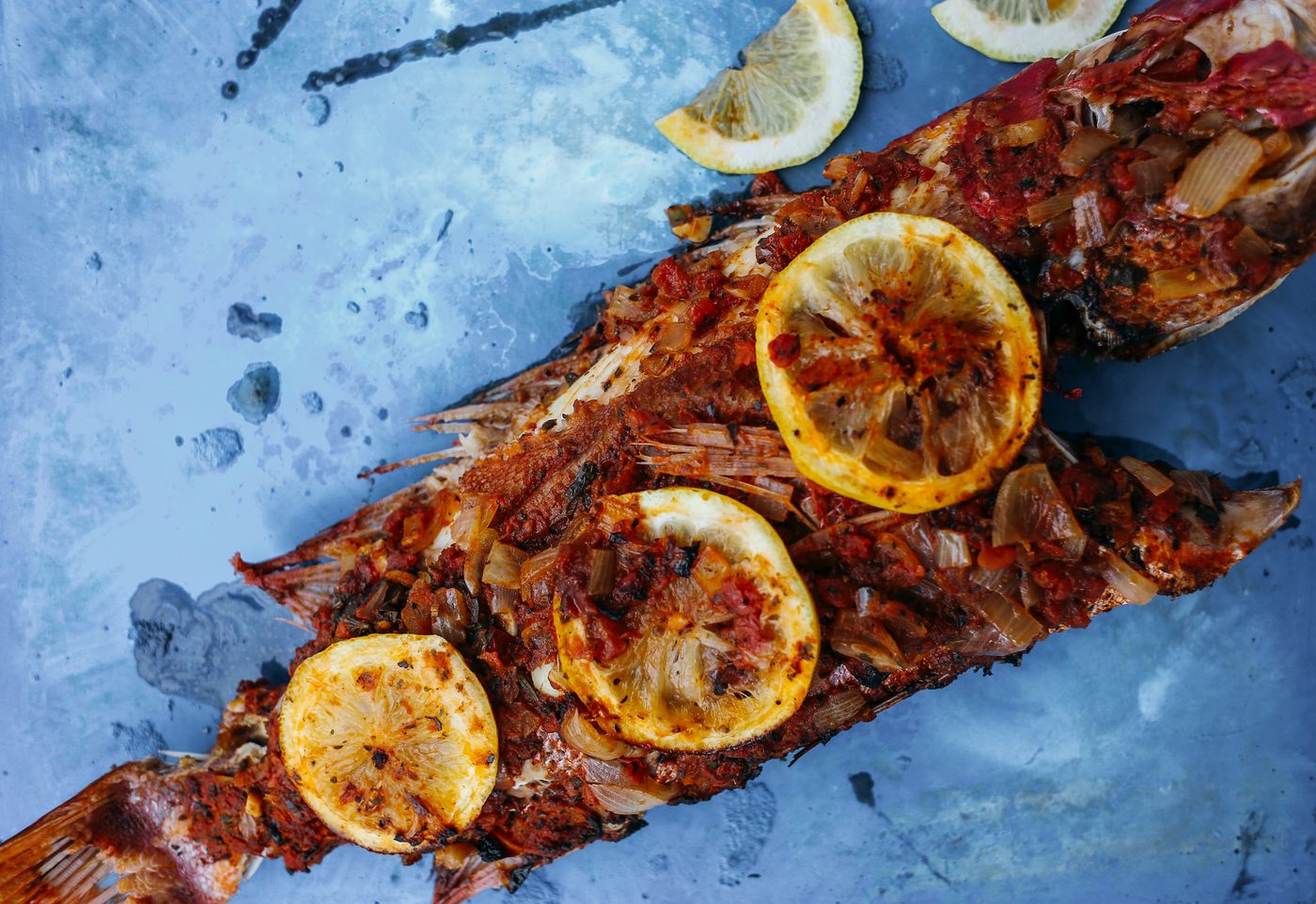 Grilled whole fish with lemon. whole grilled reddish-skinned fish; grilled lemon slices; scattered herbs.